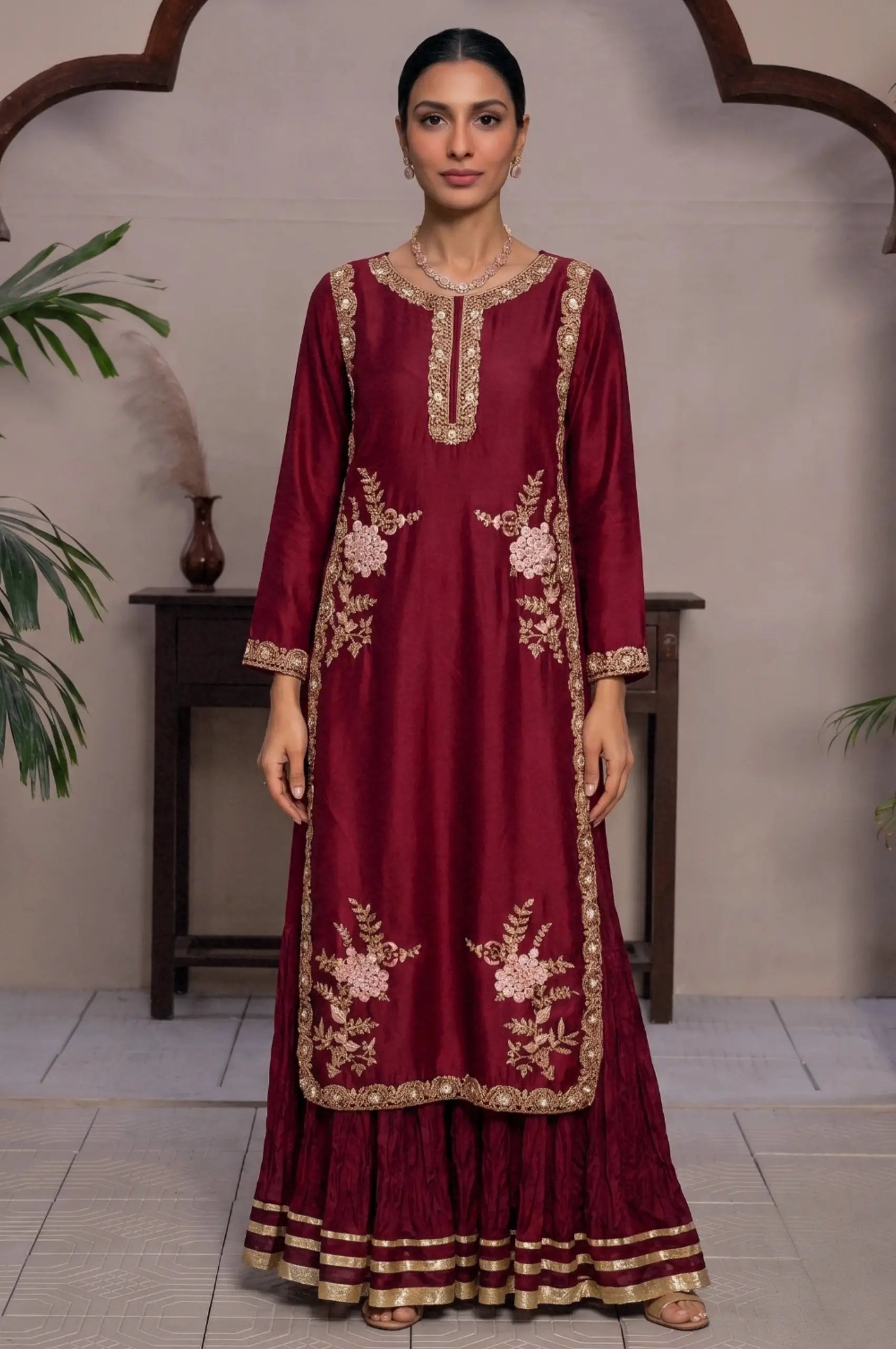 Model wearing a maroon long kurti with gold floral embroidery and a matching flared gharara.